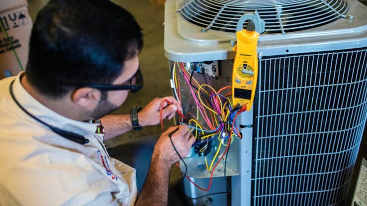 Technician testing wiring inside an outdoor air conditioning unit