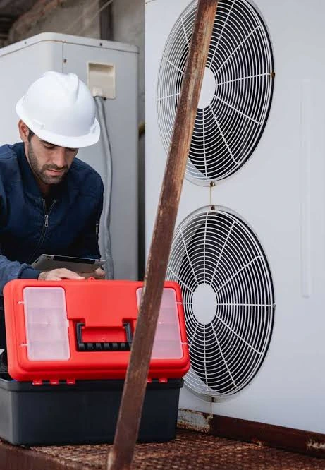 Technician inspecting outdoor HVAC equipment beside a toolbox